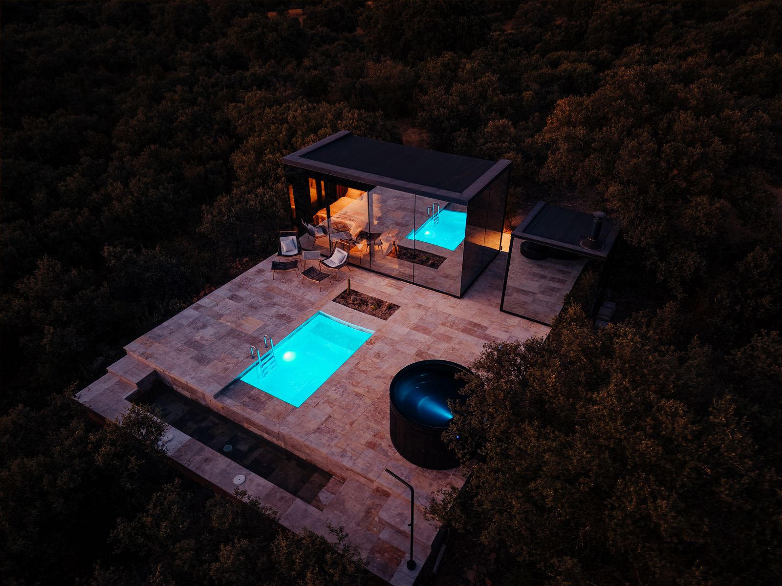 Casa Espejo de Cork Valley de noche vista desde el aire, con la piscina propia y el jacuzzi iluminados entre las encinas